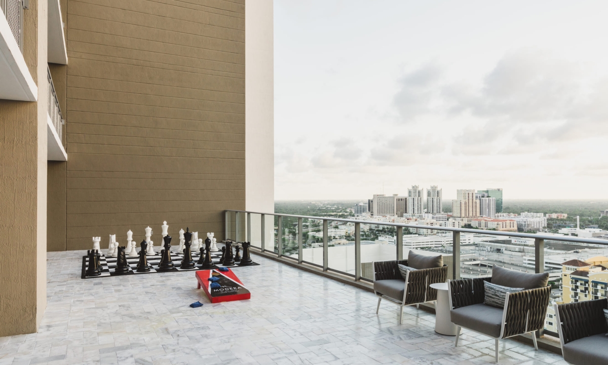 A balcony with outdoor furniture and games, overlooking a city skyline.