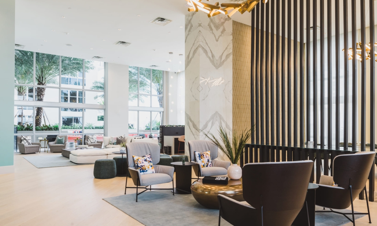 A modern hotel lobby with a seating area, large windows, and light wood flooring.